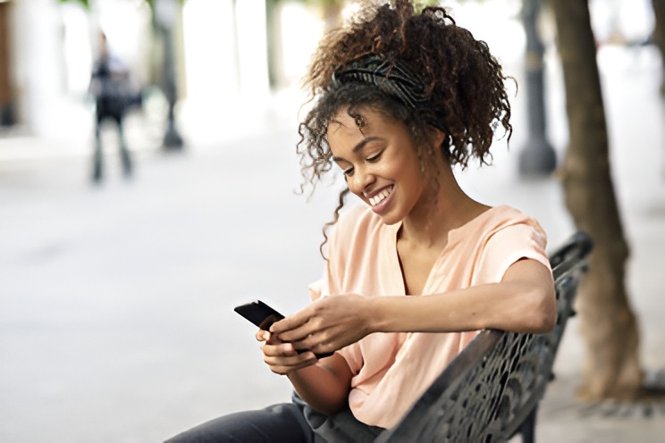 A smiling woman using a smartphone in an outdoor setting.